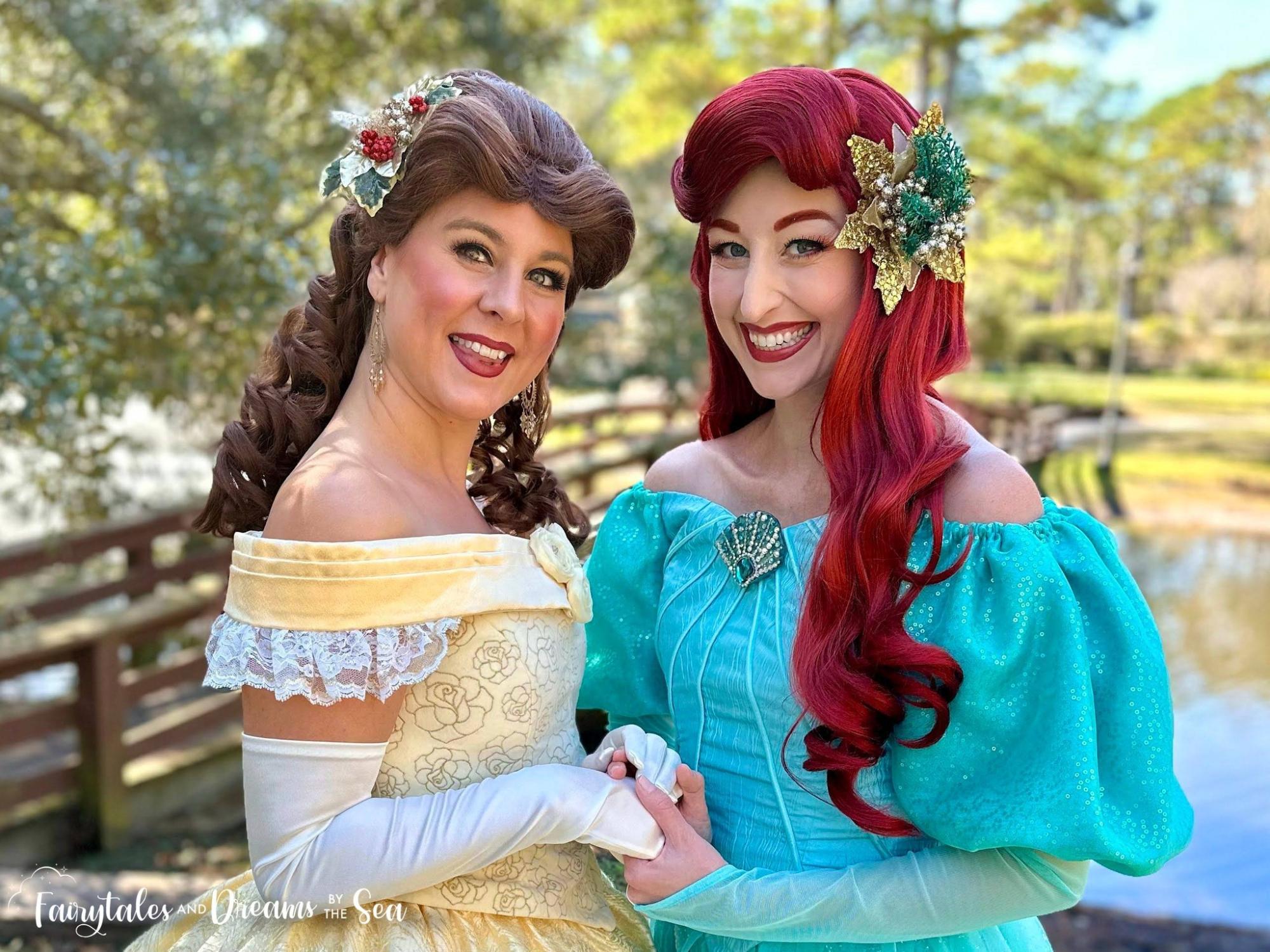 Little Mermaid and Beauty dressed in holiday attire pose in front of a bridge